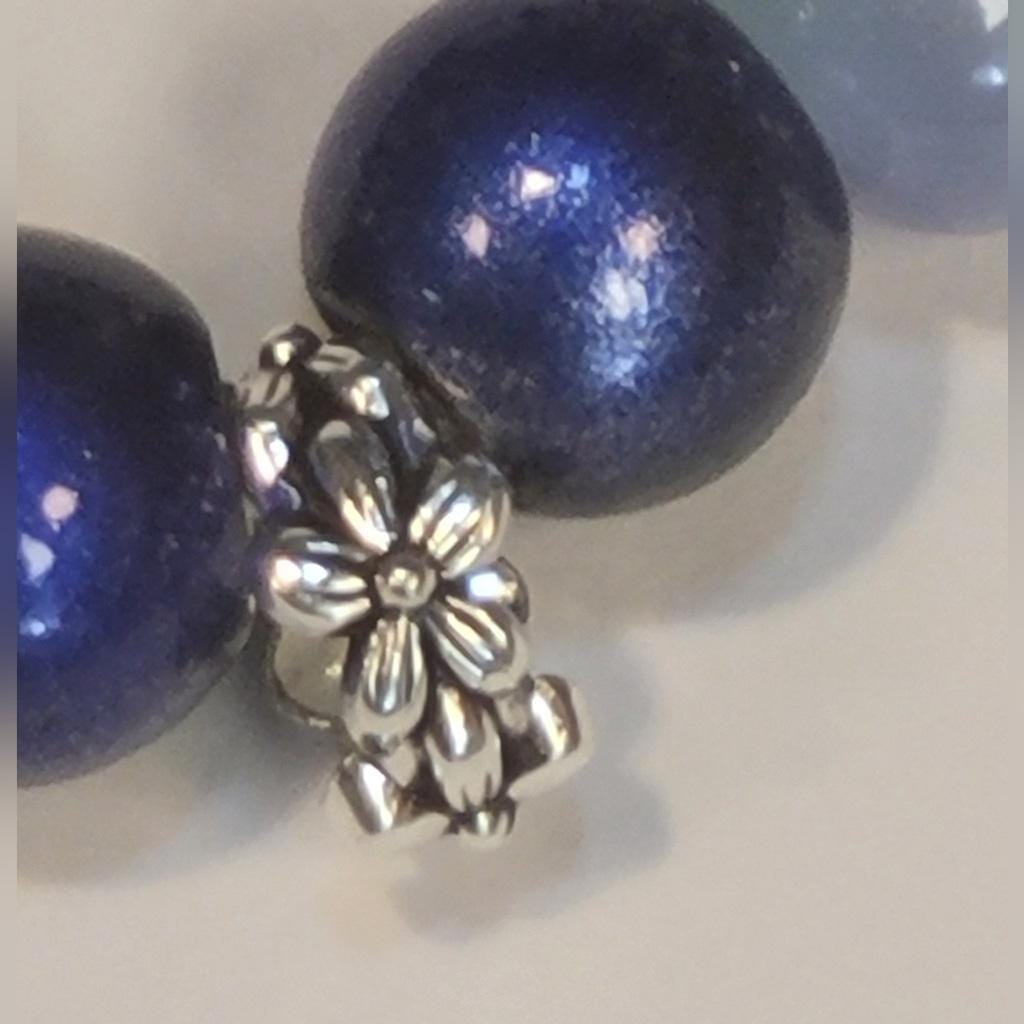 Close-up of blue beads with a silver flower-shaped  and butterfly spacer bead on a light background